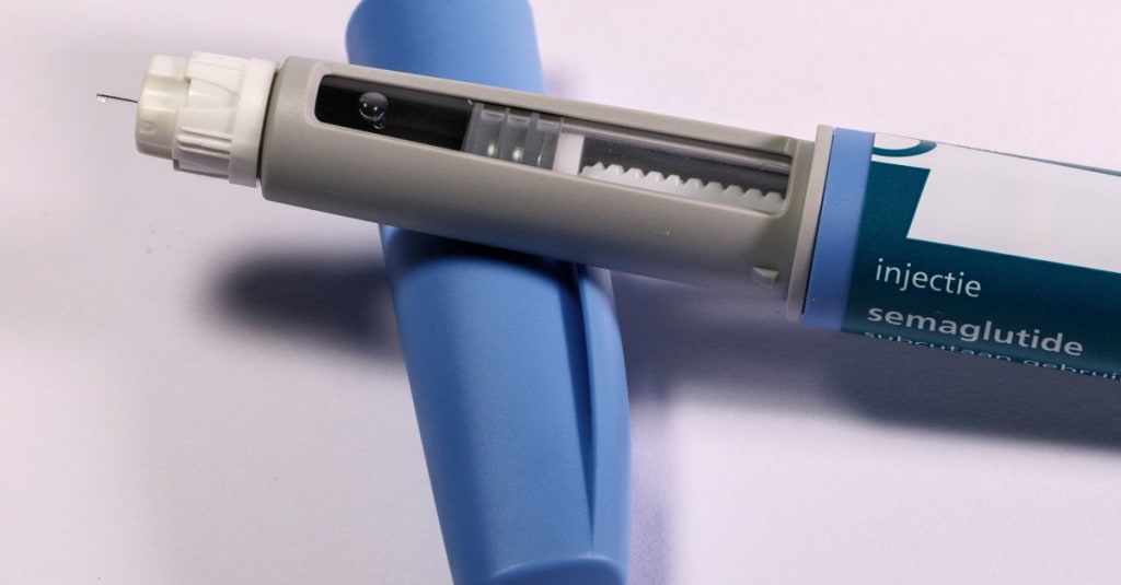 Close-up of a semaglutide injection pen with its blue cap removed, showing the needle and dosage window, on a white background.